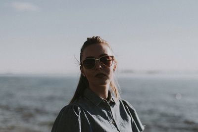 Portrait of young woman wearing sunglasses at beach against sky