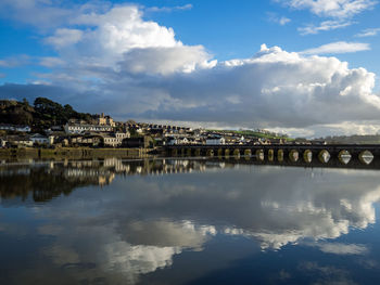 Bridge over river by buildings against sky