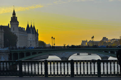 Bridge over river and buildings against sky during sunset