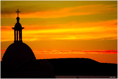 Silhouette built structure by sea against orange sky