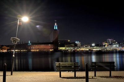 Illuminated city by river against sky at night