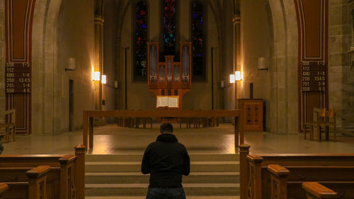 Rear view of man praying in illuminated church