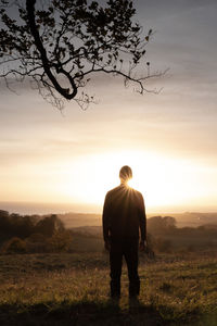 Rear view of man standing on field against sky during sunset