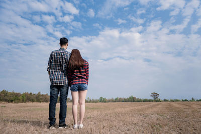 Rear view of couple standing on grassy field against sky