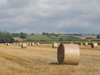 Hay bales on field against cloudy sky