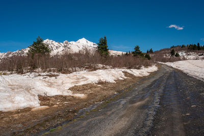 Road by snowcapped mountain against blue sky