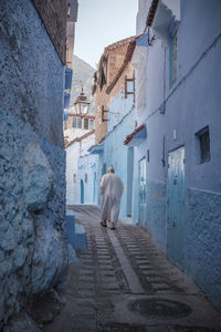 Rear view of woman walking on footpath amidst buildings