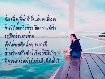 Young woman looking away while sitting on pole against sky