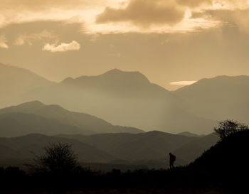 Silhouette person standing on mountain against sky during sunset