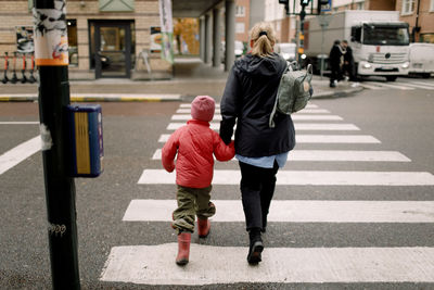 Rear view of grandmother holding hand of grandson while crossing street in city