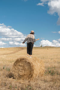 Man standing by hay bales on field against sky