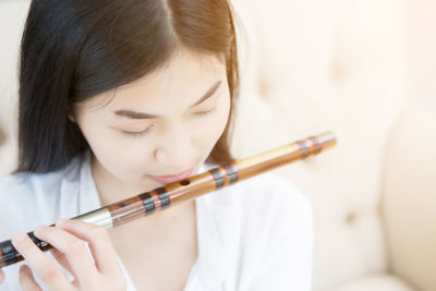 Young woman playing flute while sitting on sofa