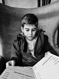 Boy reading book while sitting on sofa at home