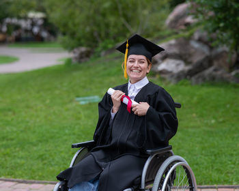 Portrait of woman wearing graduation gown standing on field