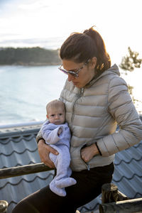 Mother carrying daughter while standing by railing against sky