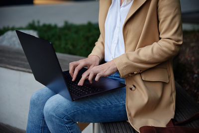 Woman sitting on bench in city street and using laptop