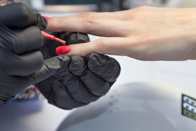 Cropped hands of manicurist applying nail polish on finger of woman
