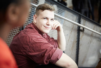 Portrait of smiling young student sitting on steps by railing at university