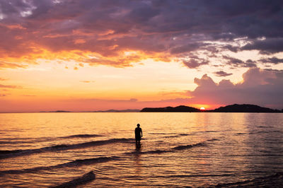 Silhouette person standing in sea against sky during sunset