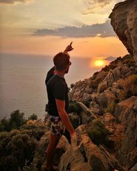 Side view of man standing on rocks at beach against sky during sunset