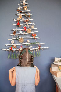 Rear view of girl by christmas tree hanging on wall