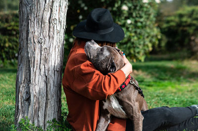 Woman embracing dog by tree trunk at park