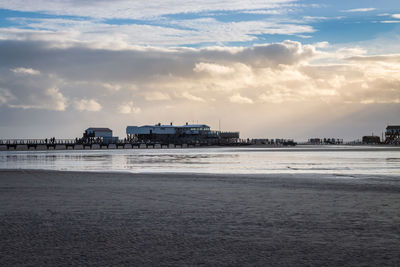 Scenic view of stilt houses and wooden seabridge at low tide north sea beach  against dramatic sky