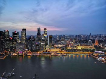 Illuminated buildings by river against sky in city