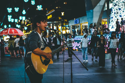 Side view of singer playing guitar on street at night