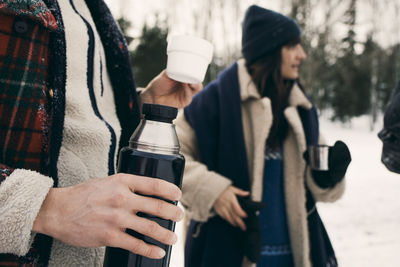 Midsection of man having coffee with friends at park during winter