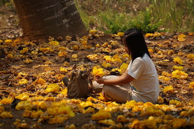 Side view of woman sitting on autumn leaves