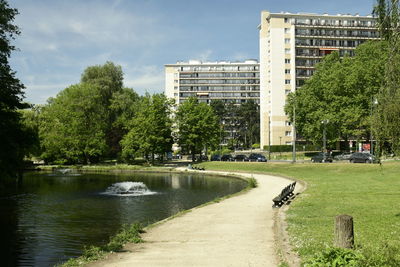 Trees by lake in park against buildings in city