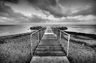 Wooden pier leading towards sea against sky