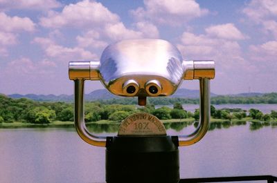 Coin-operated binoculars by river against sky