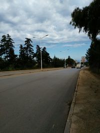 Empty road by trees against sky