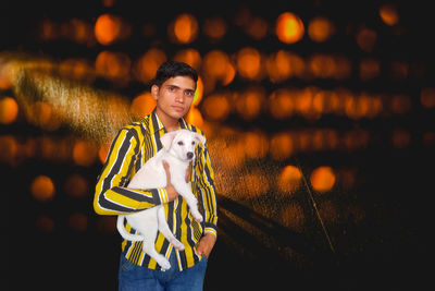 Portrait of young man holding puppy against light beams on wall