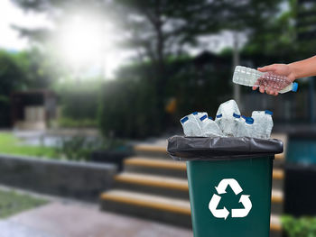 Close-up of person putting plastic bottle in garbage bin