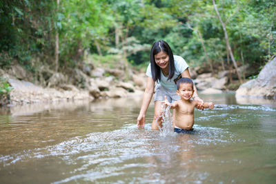 Happy mother with son standing in river at forest