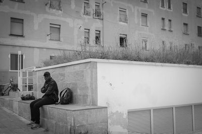 Full length of man sitting by building in city