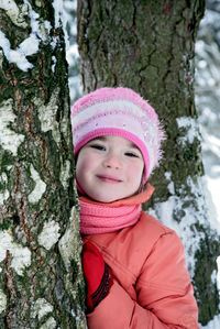 Portrait of happy girl hiding behind tree trunk in winter