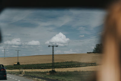 Road by electricity pylon on field against sky