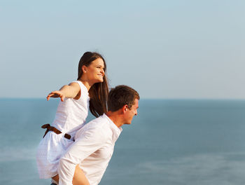 Man giving piggyback ride to woman against sky