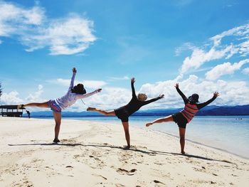 Rear view of people standing on one leg at beach against sky