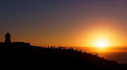 Silhouette people by sea against sky during sunset