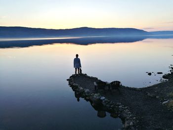 Rear view of woman standing by calm lake during sunset