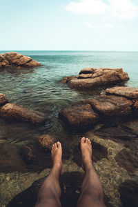 Low section of person on rock by sea against sky