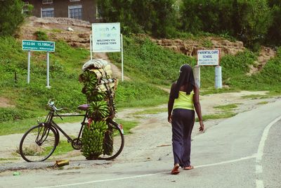 Rear view of woman walking by bicycles with bananas on roadside