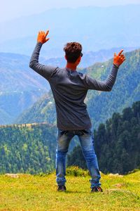 Rear view of man with arms raised standing against mountains