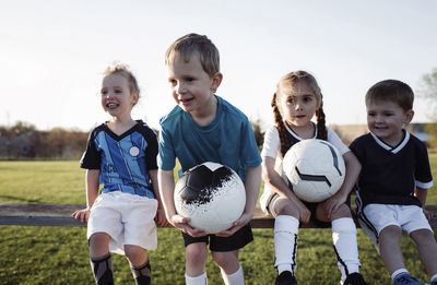 Children looking away while sitting on bench against clear sky at park during sunset