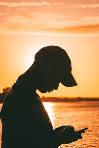 Rear view of silhouette woman standing at beach against sky during sunset